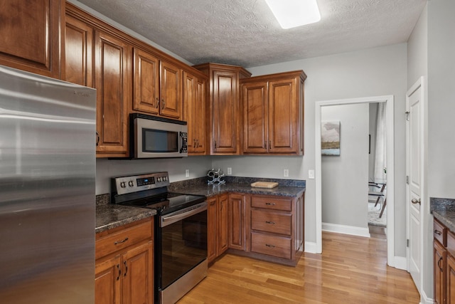 kitchen featuring appliances with stainless steel finishes, light hardwood / wood-style floors, a textured ceiling, and dark stone counters