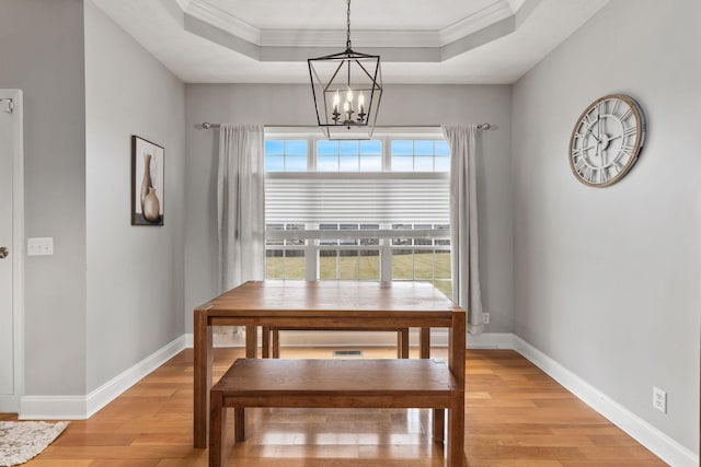 dining area featuring ornamental molding, a notable chandelier, light hardwood / wood-style floors, and a tray ceiling