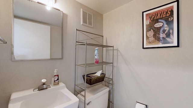 half bath with toilet, a sink, and visible vents