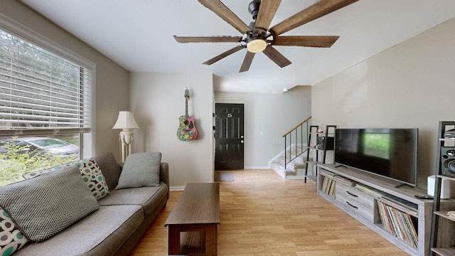 living area featuring light wood finished floors, stairs, baseboards, and a ceiling fan