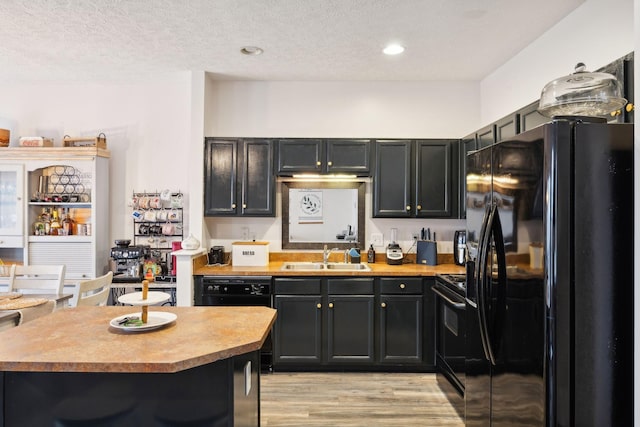 kitchen with sink, light hardwood / wood-style flooring, black appliances, a textured ceiling, and a kitchen bar