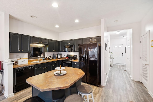 kitchen featuring sink, a breakfast bar, black appliances, a kitchen island, and light wood-type flooring