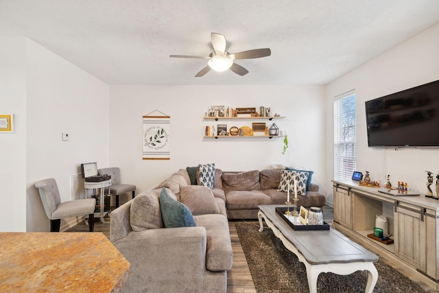 living room featuring dark wood-type flooring, ceiling fan, and a textured ceiling