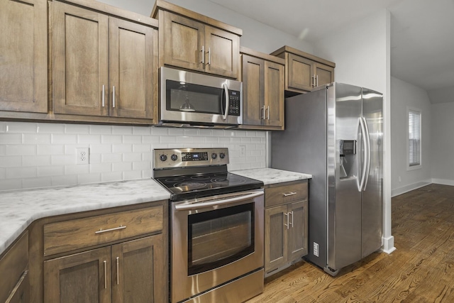 kitchen featuring appliances with stainless steel finishes, light stone countertops, light hardwood / wood-style floors, and backsplash