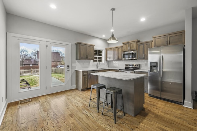 kitchen featuring stainless steel appliances, decorative light fixtures, a kitchen island, and light wood-type flooring