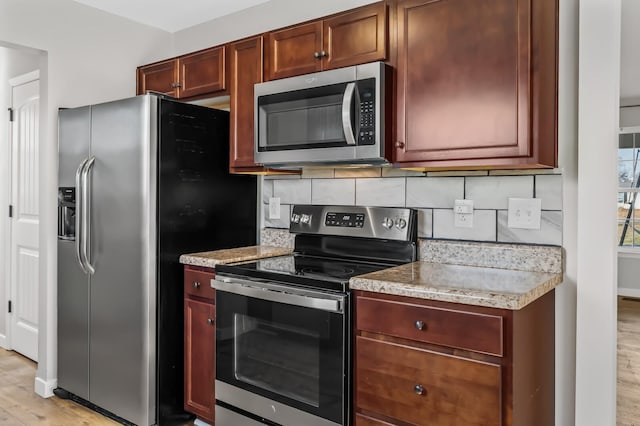 kitchen with appliances with stainless steel finishes, light wood-style flooring, and tasteful backsplash