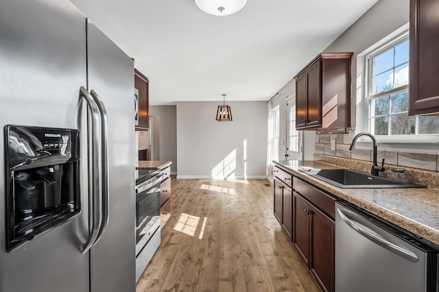 kitchen with light wood finished floors, dark countertops, appliances with stainless steel finishes, pendant lighting, and a sink