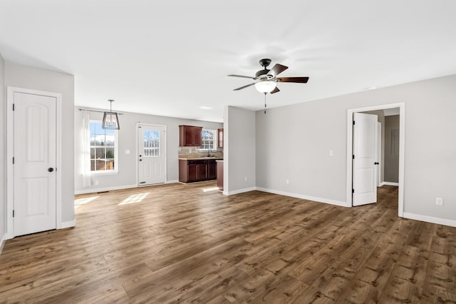 unfurnished living room with ceiling fan, dark wood-type flooring, a sink, and baseboards