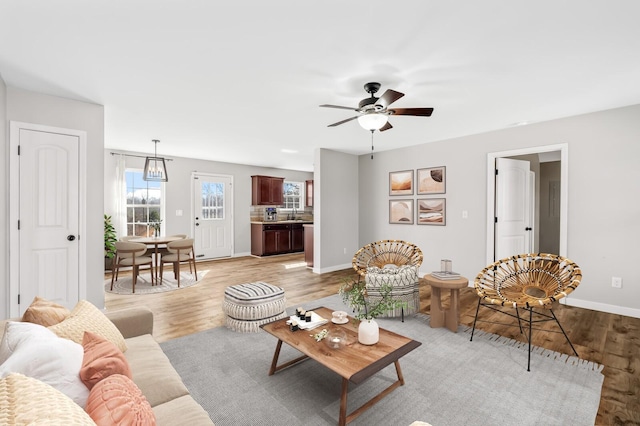 living area featuring light wood-style floors, baseboards, and a ceiling fan