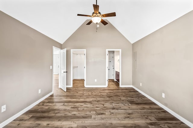 unfurnished bedroom with baseboards, dark wood finished floors, connected bathroom, a walk in closet, and high vaulted ceiling