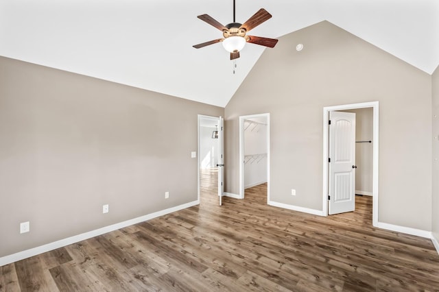 unfurnished bedroom with high vaulted ceiling, a walk in closet, dark wood-style flooring, and baseboards