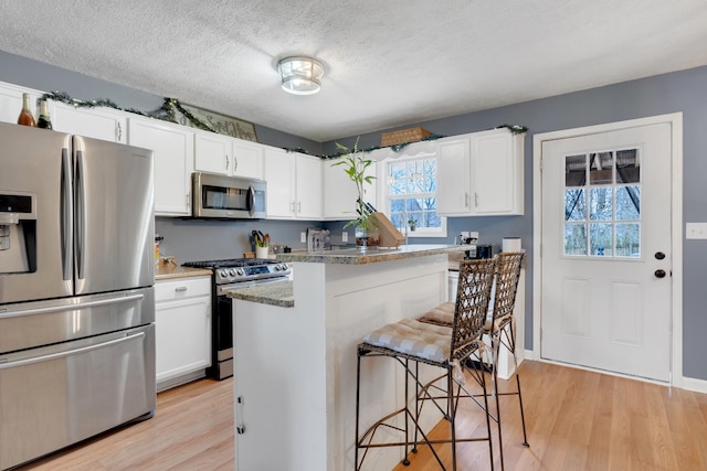 kitchen with a breakfast bar area, white cabinetry, appliances with stainless steel finishes, dark stone counters, and light hardwood / wood-style floors