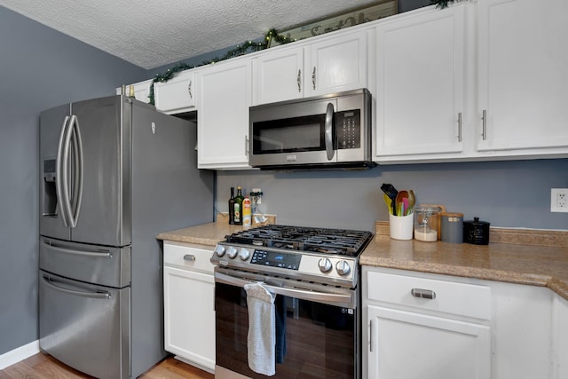 kitchen with appliances with stainless steel finishes, light wood-type flooring, white cabinets, and a textured ceiling