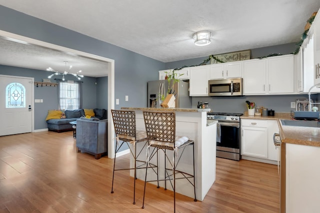 kitchen featuring an inviting chandelier, light hardwood / wood-style flooring, a kitchen breakfast bar, stainless steel appliances, and white cabinets