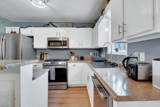 kitchen with sink, a textured ceiling, stainless steel appliances, light hardwood / wood-style floors, and white cabinets