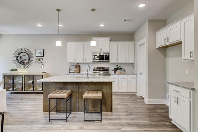 kitchen with sink, appliances with stainless steel finishes, white cabinetry, light stone counters, and an island with sink