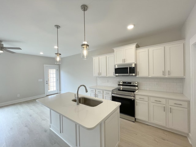 kitchen featuring pendant lighting, sink, white cabinetry, stainless steel appliances, and an island with sink