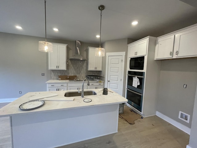 kitchen with white cabinets, a center island with sink, hanging light fixtures, and wall chimney range hood