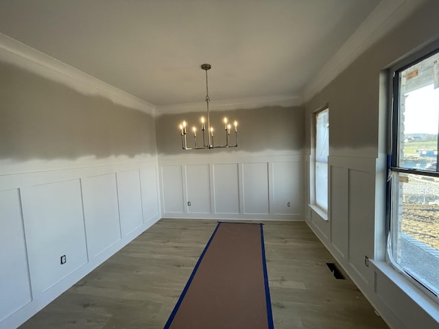 unfurnished dining area featuring crown molding, hardwood / wood-style floors, and a notable chandelier