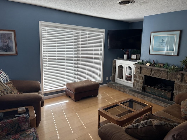 living room with a stone fireplace and a textured ceiling