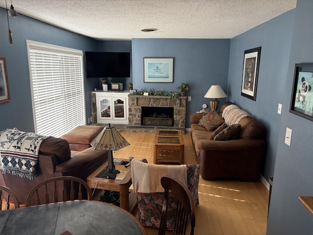 living room featuring a stone fireplace, light hardwood / wood-style flooring, and a textured ceiling