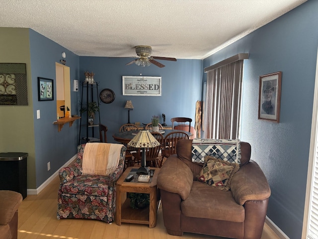 living room featuring ceiling fan, a textured ceiling, and light wood-type flooring