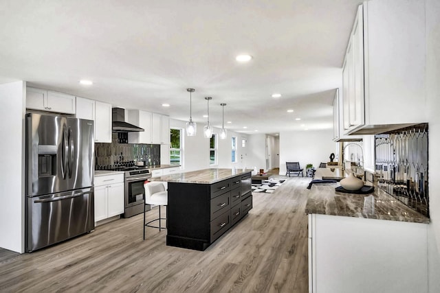 kitchen with white cabinetry, decorative light fixtures, appliances with stainless steel finishes, a large island, and wall chimney range hood