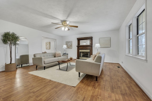 living room with ceiling fan, a textured ceiling, and light wood-type flooring