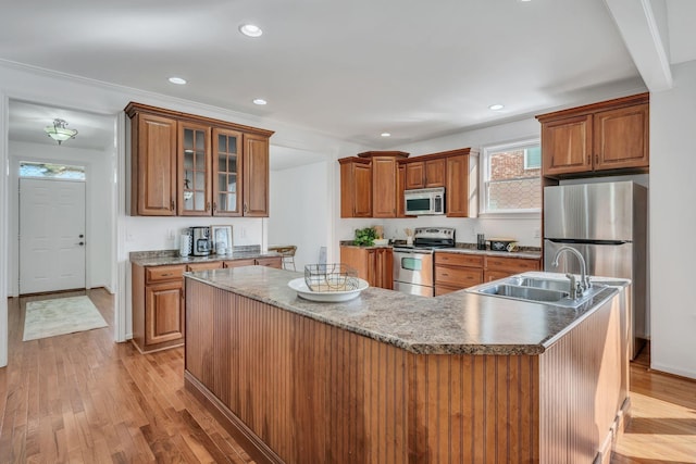 kitchen with appliances with stainless steel finishes, light hardwood / wood-style floors, sink, and a center island with sink