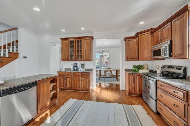 kitchen with crown molding, stainless steel appliances, light stone counters, a chandelier, and light wood-type flooring