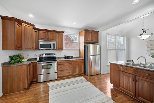 kitchen featuring stainless steel appliances, hanging light fixtures, sink, and light hardwood / wood-style flooring