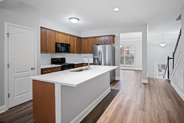 kitchen with sink, backsplash, black appliances, a center island with sink, and decorative light fixtures