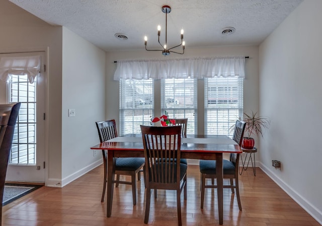 dining area with a notable chandelier, wood-type flooring, a textured ceiling, and a wealth of natural light