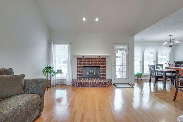 living room with a fireplace, a chandelier, vaulted ceiling, and light hardwood / wood-style flooring