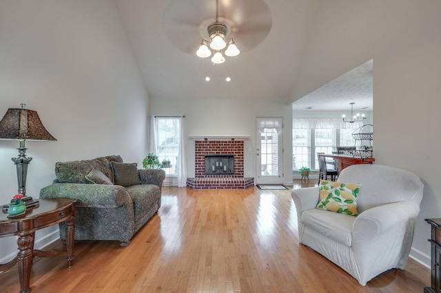 living room with ceiling fan with notable chandelier, a fireplace, high vaulted ceiling, and light wood-type flooring