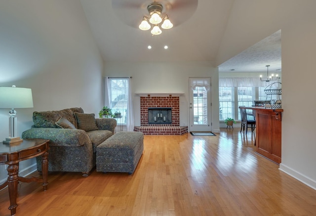 living room featuring ceiling fan, high vaulted ceiling, a fireplace, and light wood-type flooring