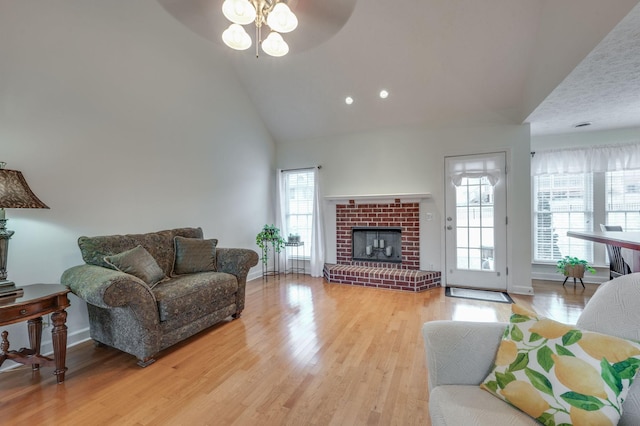 living room featuring ceiling fan, high vaulted ceiling, light hardwood / wood-style floors, and a brick fireplace