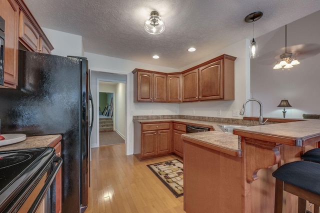 kitchen featuring sink, a kitchen bar, hanging light fixtures, kitchen peninsula, and light wood-type flooring