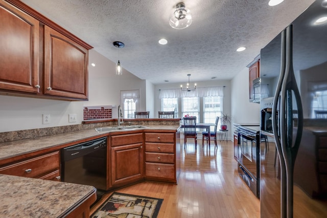 kitchen featuring sink, light wood-type flooring, kitchen peninsula, pendant lighting, and black appliances