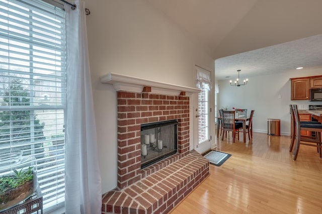 living room featuring lofted ceiling, a fireplace, a chandelier, and light hardwood / wood-style flooring