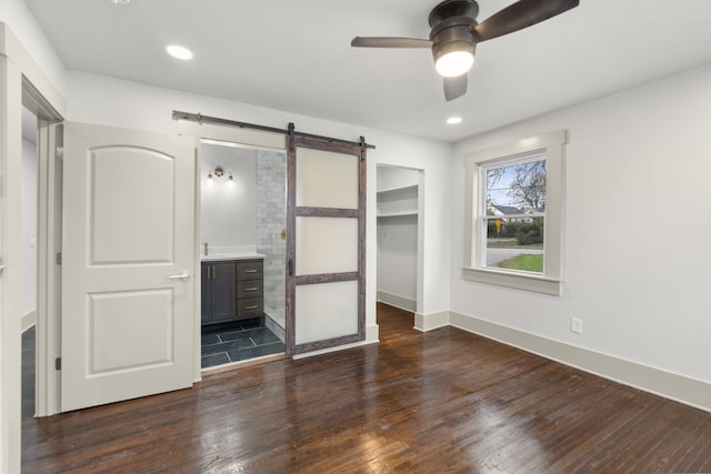 unfurnished bedroom with ensuite bathroom, a walk in closet, a barn door, dark wood-type flooring, and a closet