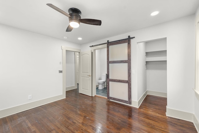 unfurnished bedroom featuring dark hardwood / wood-style floors, ensuite bathroom, a barn door, a walk in closet, and a closet