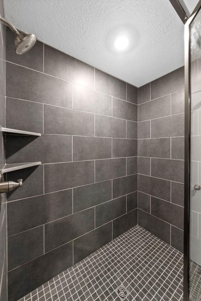 bathroom with a textured ceiling and a tile shower