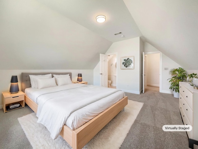 bedroom featuring light colored carpet, lofted ceiling, and ensuite bath