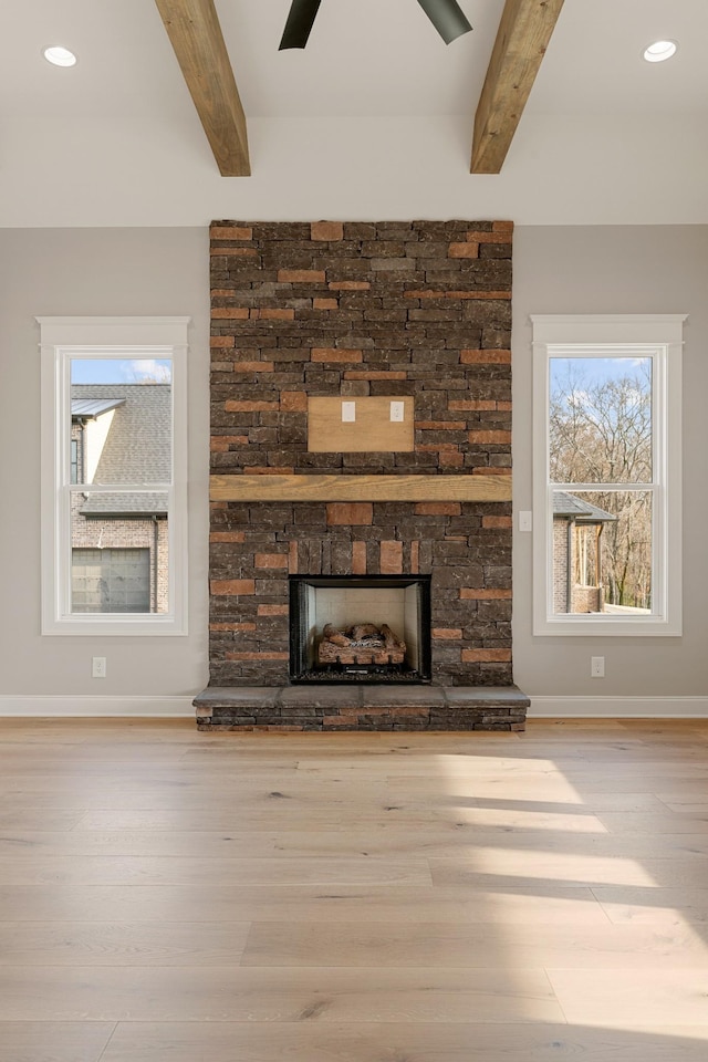 unfurnished living room featuring ceiling fan, a stone fireplace, beamed ceiling, and light wood-type flooring