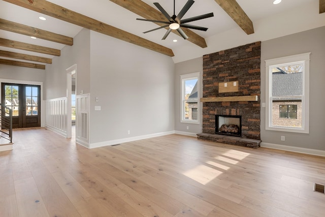 unfurnished living room featuring ceiling fan, a stone fireplace, french doors, beamed ceiling, and light wood-type flooring