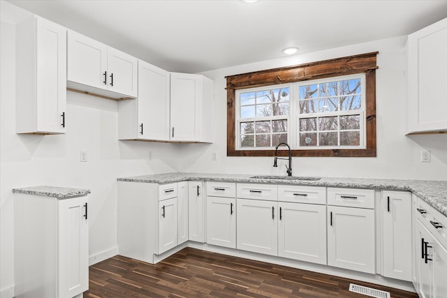 kitchen featuring dark hardwood / wood-style floors, light stone countertops, sink, and white cabinets