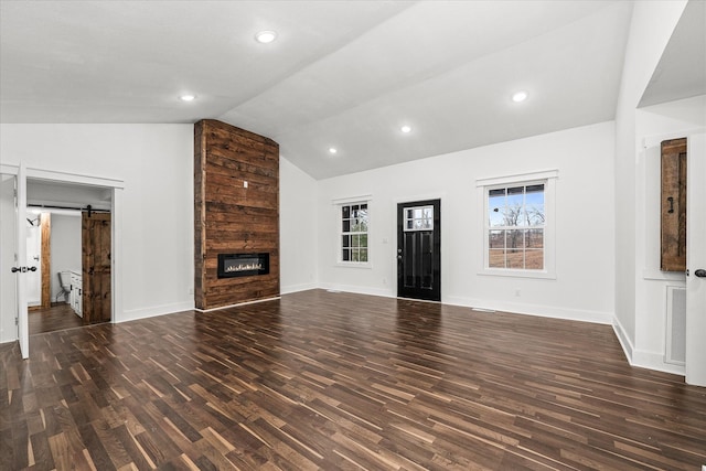 unfurnished living room featuring a barn door, a large fireplace, lofted ceiling, and dark hardwood / wood-style floors