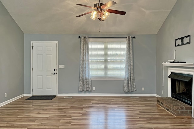 unfurnished living room featuring a brick fireplace, hardwood / wood-style flooring, vaulted ceiling, and ceiling fan