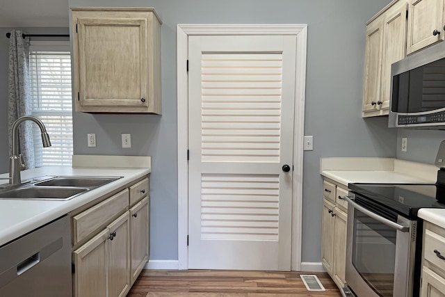 kitchen featuring light brown cabinetry, sink, wood-type flooring, and appliances with stainless steel finishes